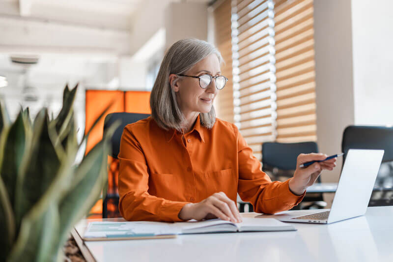 Middle-aged woman working on a laptop. Growth Heroes - business experts