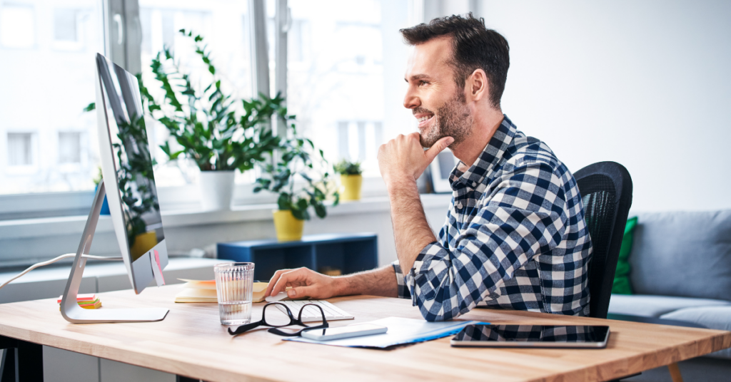 The image shows a middle-aged man working from home in a bright office with a desktop computer.