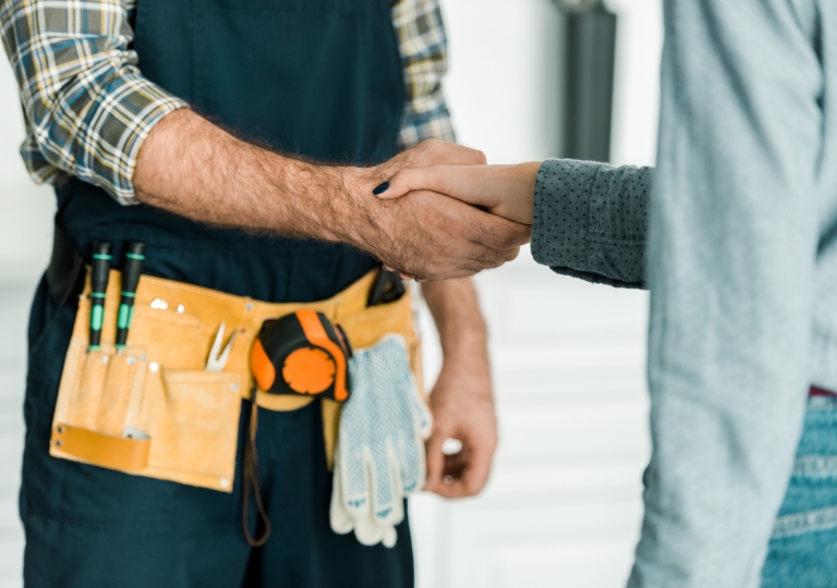 A service representative with a toolbelt shakes hands with a customer onsite.